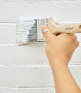 Hand with brush painting a white brick wall.