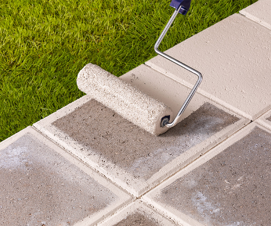 Concrete walkway across grass lawn being sealed by roller with white sealer.