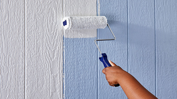 Hand with large roller painting white over light blue paneling. 