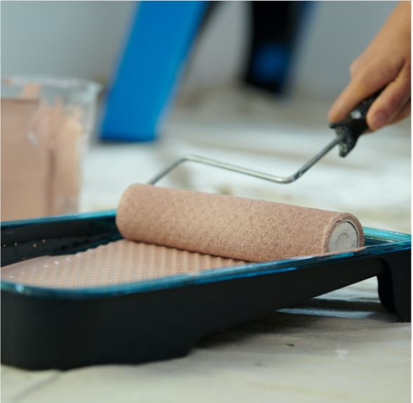 Roller picking up almond-hued paint from a paint tray. Tray sits on drop cloth.