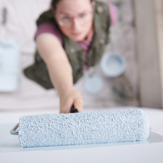 Overhead shot of woman stretching to roll paint on wall.