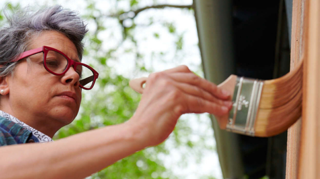 A woman using a brush to stain an exterior door frame.