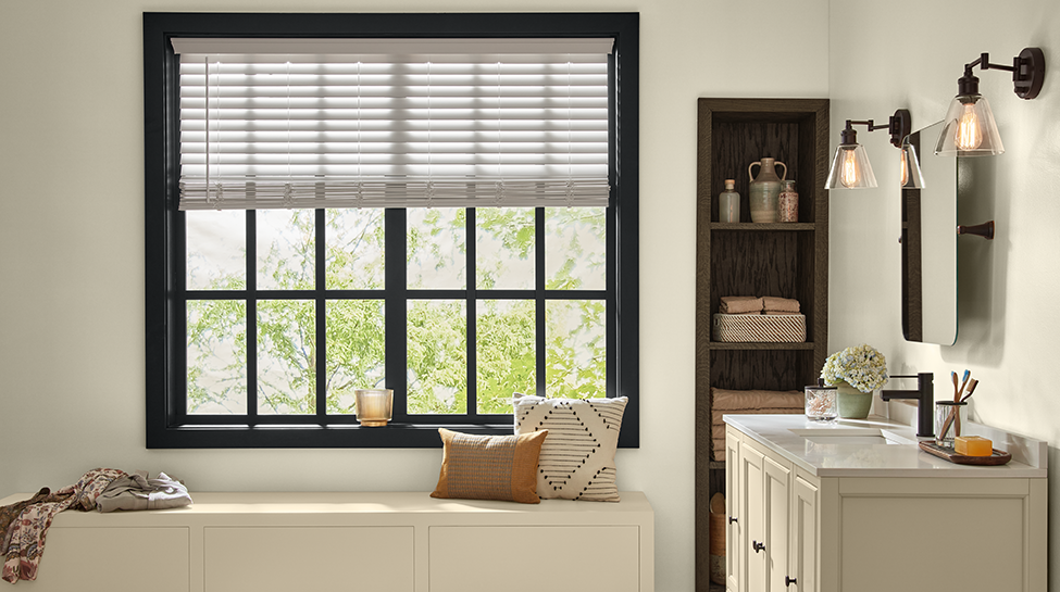 Bathroom with window, vanity, light fixtures, drawer with pillows on it, shelf with towels and candle on window sill. 