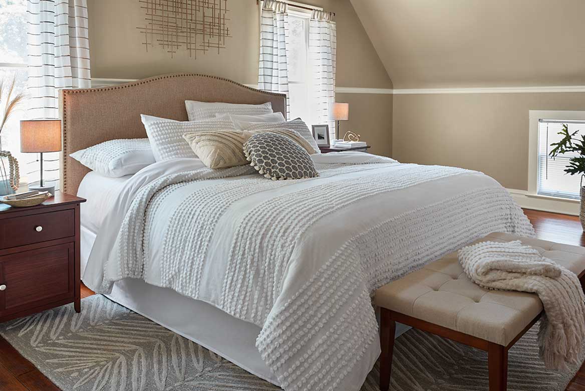 Bedroom with warm gray walls and bed between two windows. Light neutral trim runs mid-height around the room.