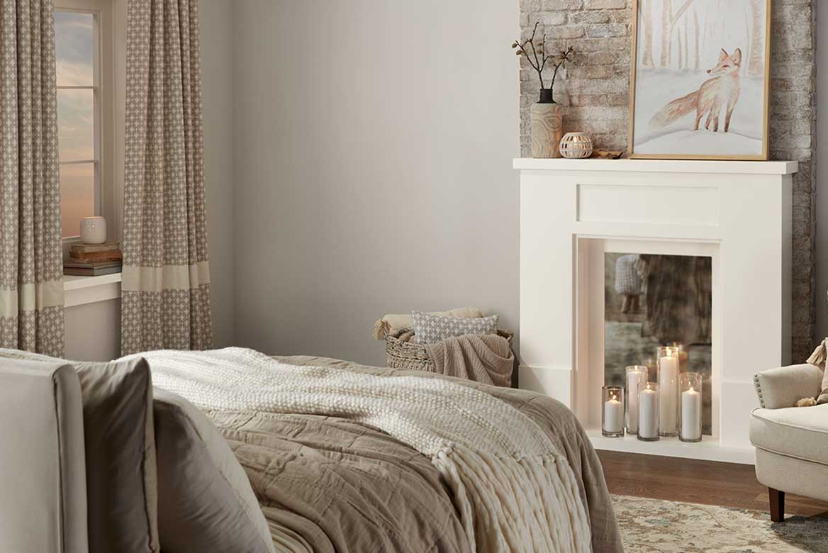 Near-monochromatic bedroom of gray-and-neutrals palette with mirrored fireplace and glass-enclosed candles.