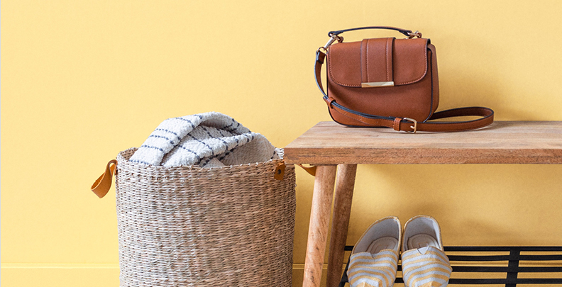 Entryway in Sunglow features a large woven basket and shoe bench upon which rests a leather purse. 