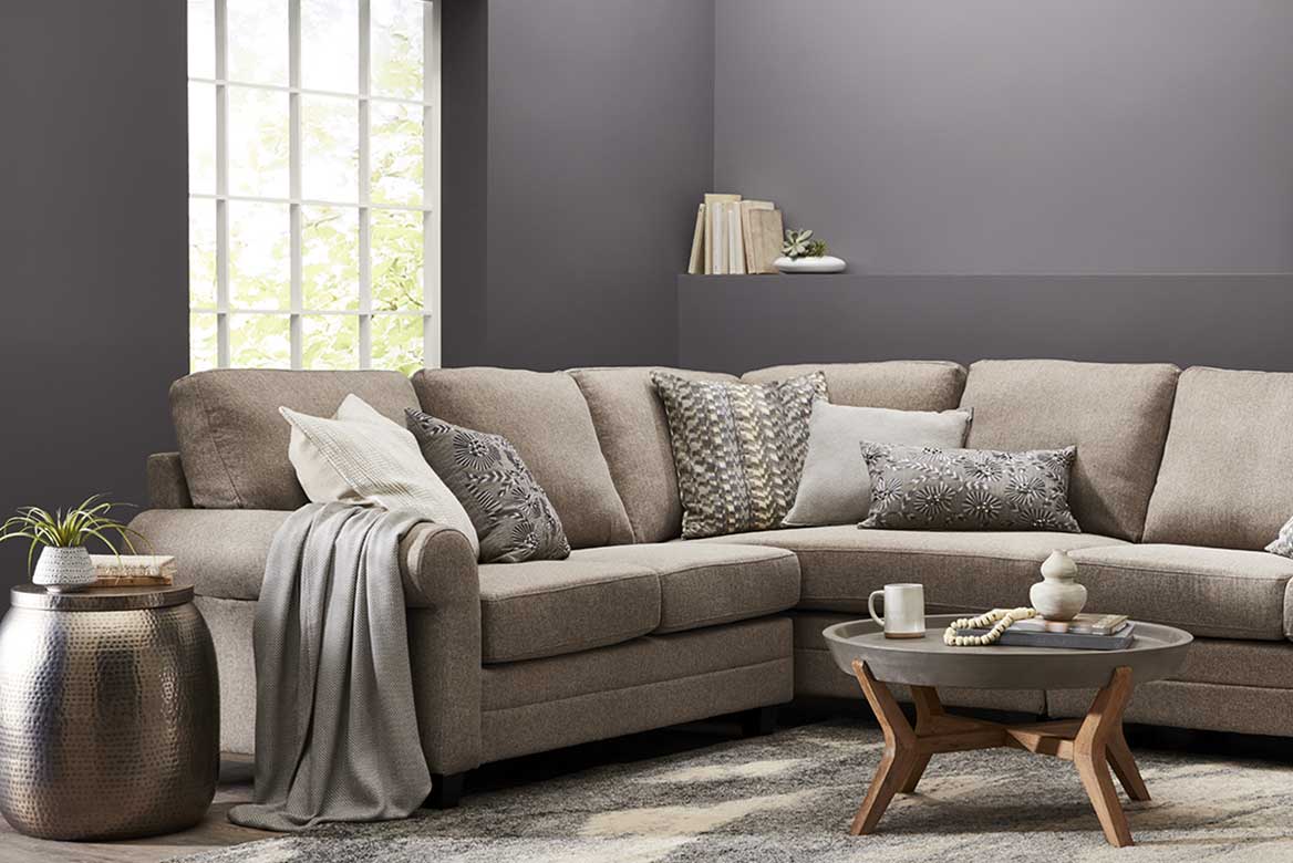 Deep neutral sectional in corner against warm gray wall with tall, paned windows and built-in shelf.