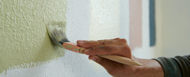 Painting wall green with brush. Color swatches on wall in background.