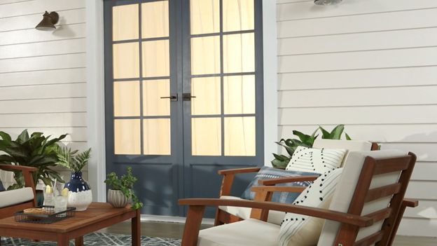 Patio with wood chairs and table holding decorative items with plants, French doors and a light fixture in background.