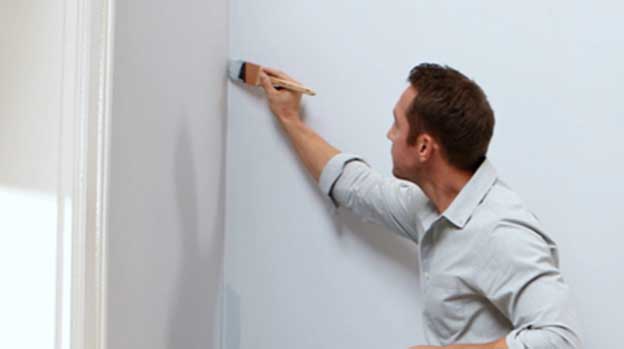 Man painting seam at corner of a wall with a brush.