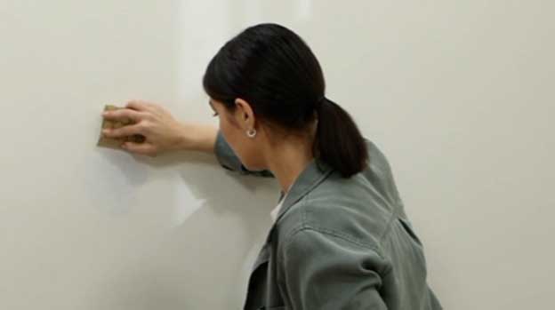 Woman sanding portion of wall to prep for priming or painting.