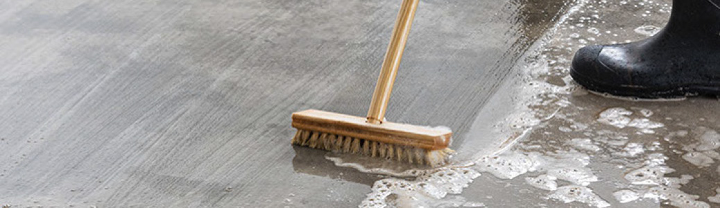 Push broom clearing liquid off concrete floor. Rubber boots in background.