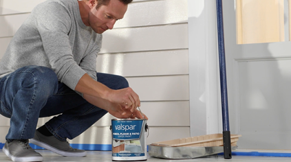 Person squatting and opening a can in a taped-off area with a tray and blue extension handle.